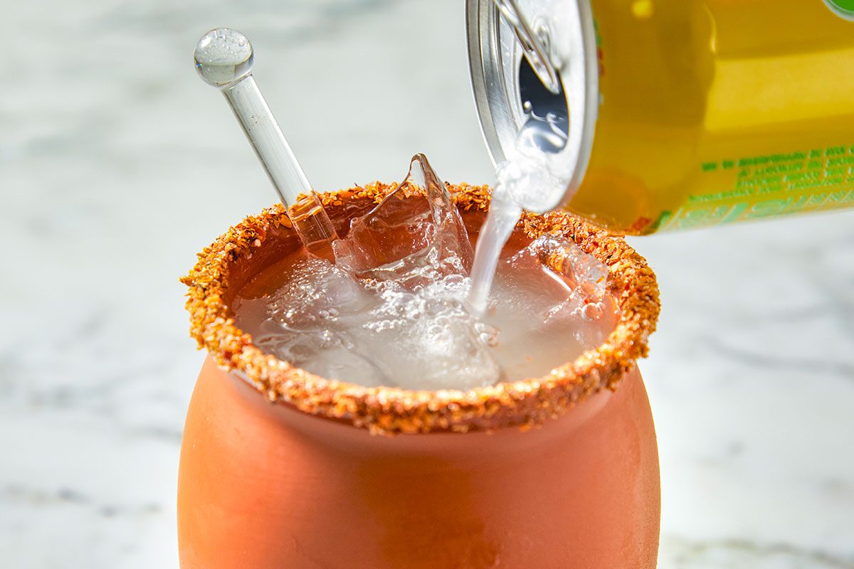 Grapefruit soda is poured into the ice-filled, Tajín-rimmed glass to top off the cocktail.