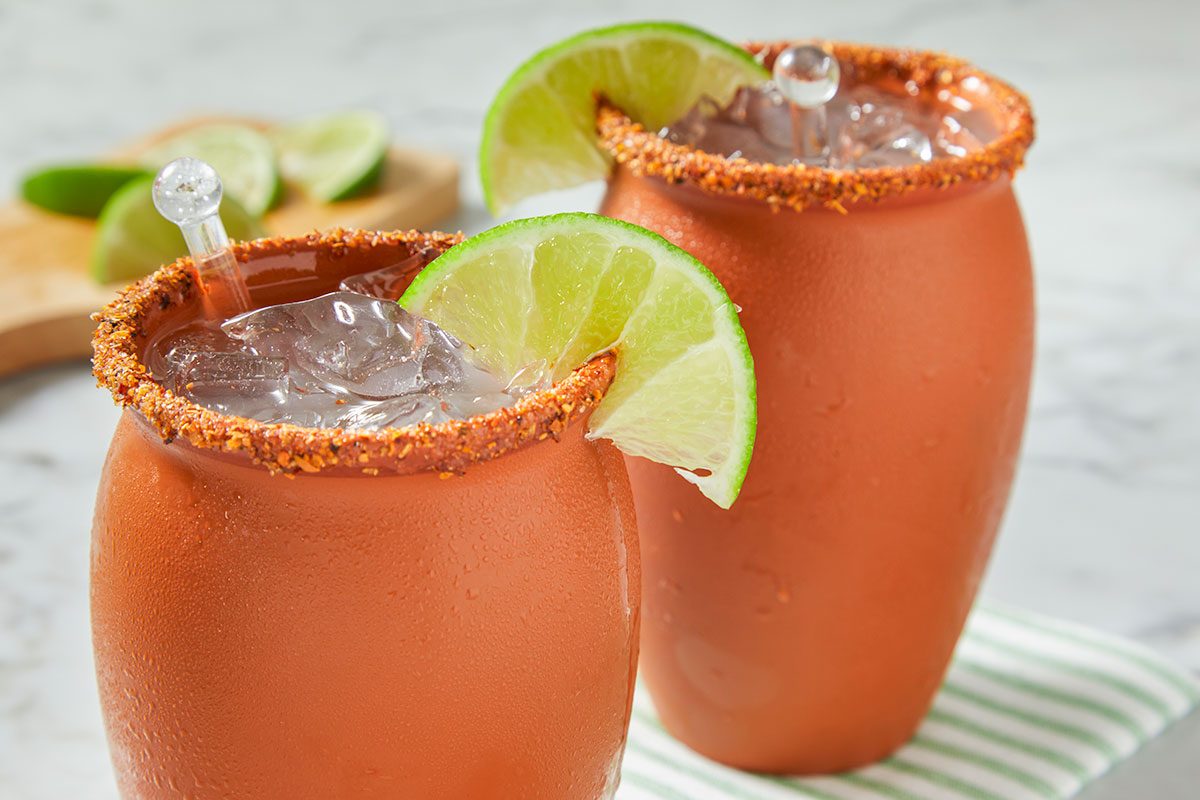 Two finished cantarito cocktails are served together with lime wedges, showcasing a refreshing citrus presentation.