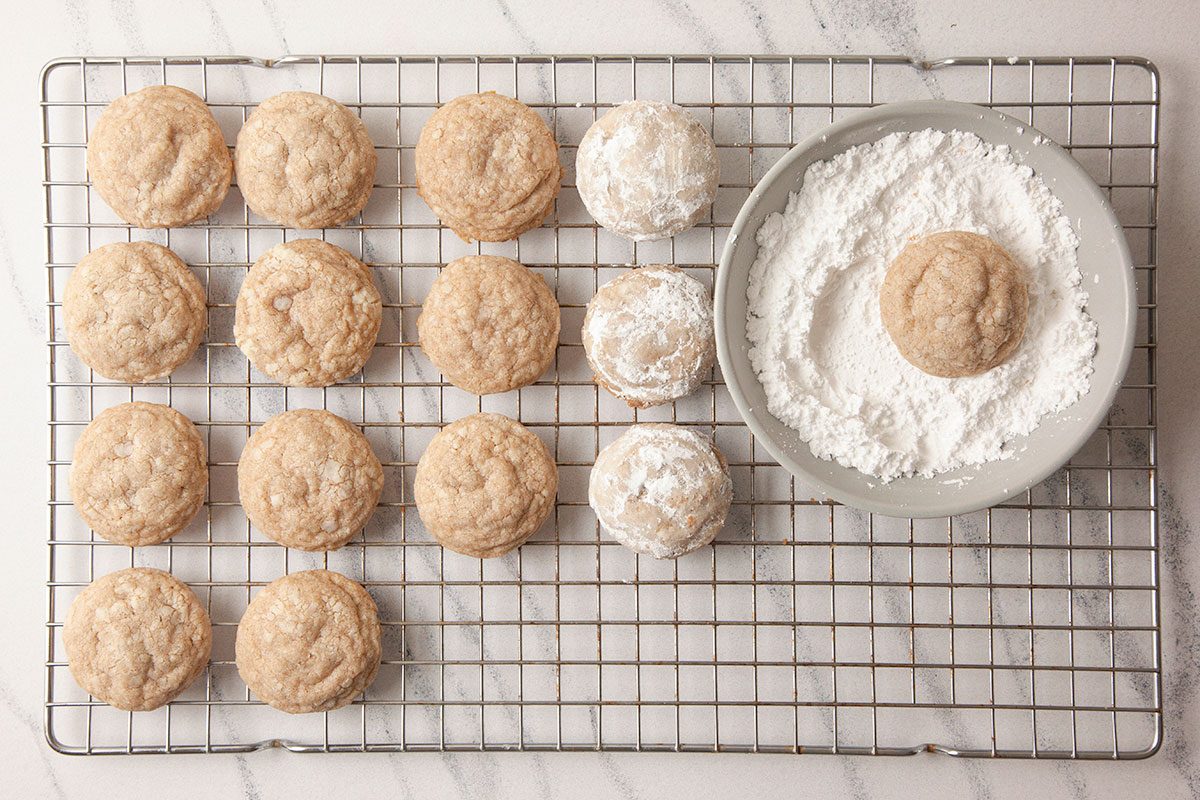 A vertical overhead image shows evenly portioned cookie dough balls arranged on a wire rack with a bowl of powdered sugar nearby.