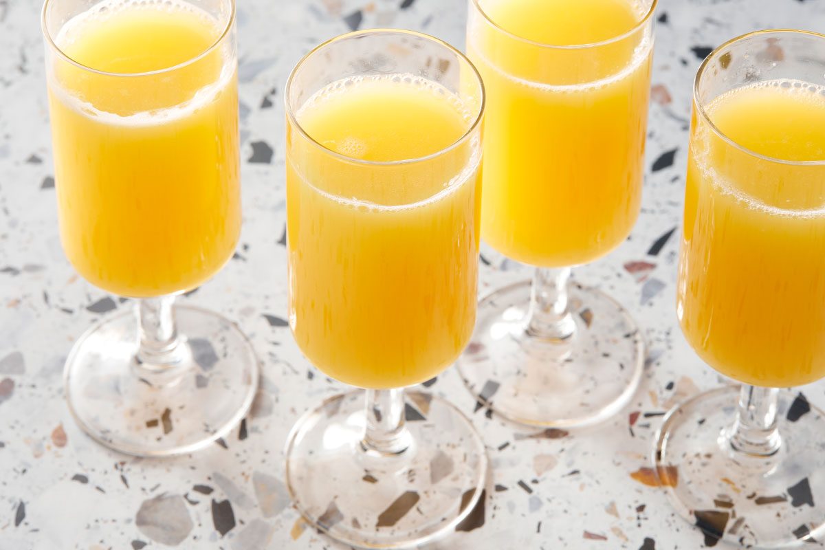 A horizontal image shows multiple glasses of mimosas grouped together with bright orange tones.