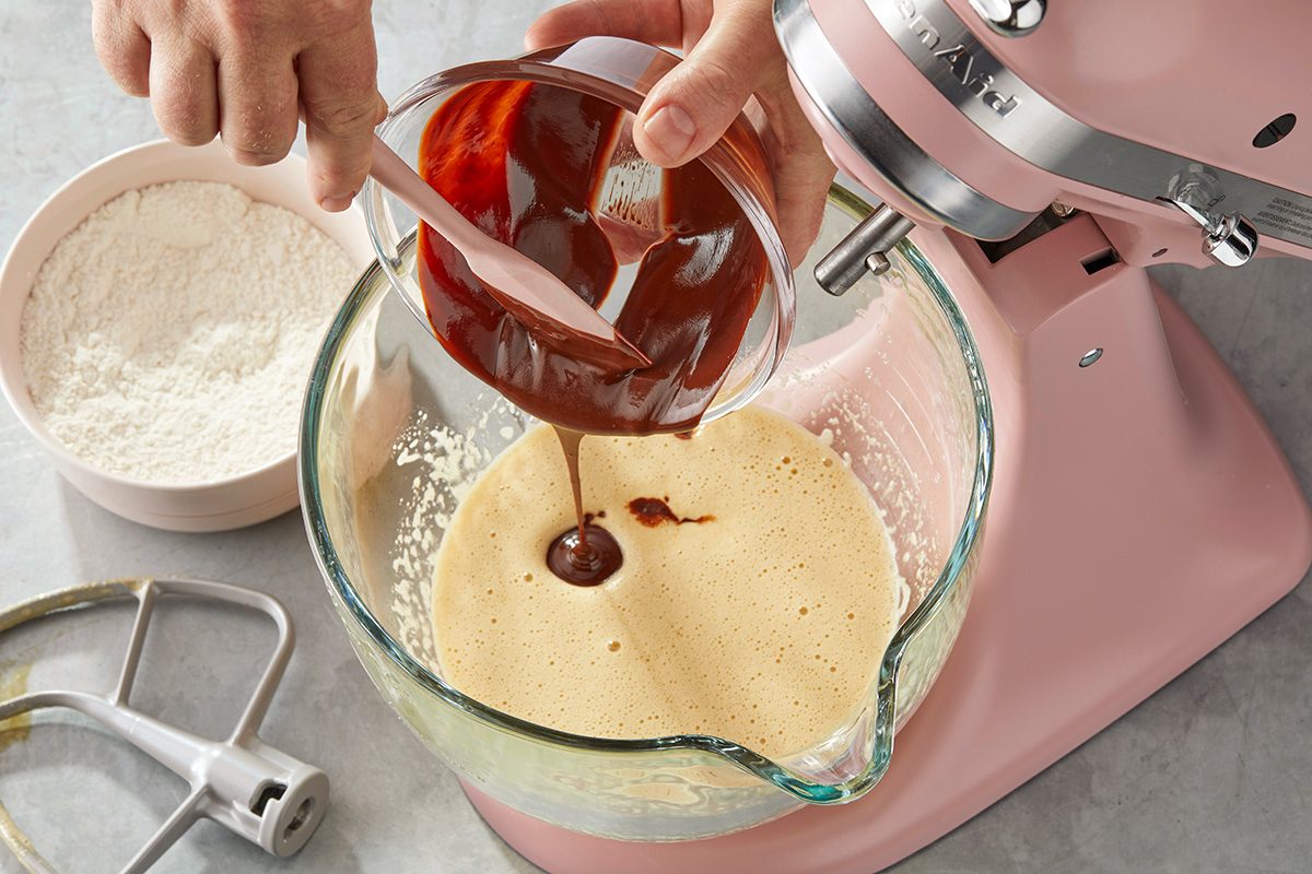 Pouring a red-brown sauce with a pink spatula into a bowl of tan dough mixture
