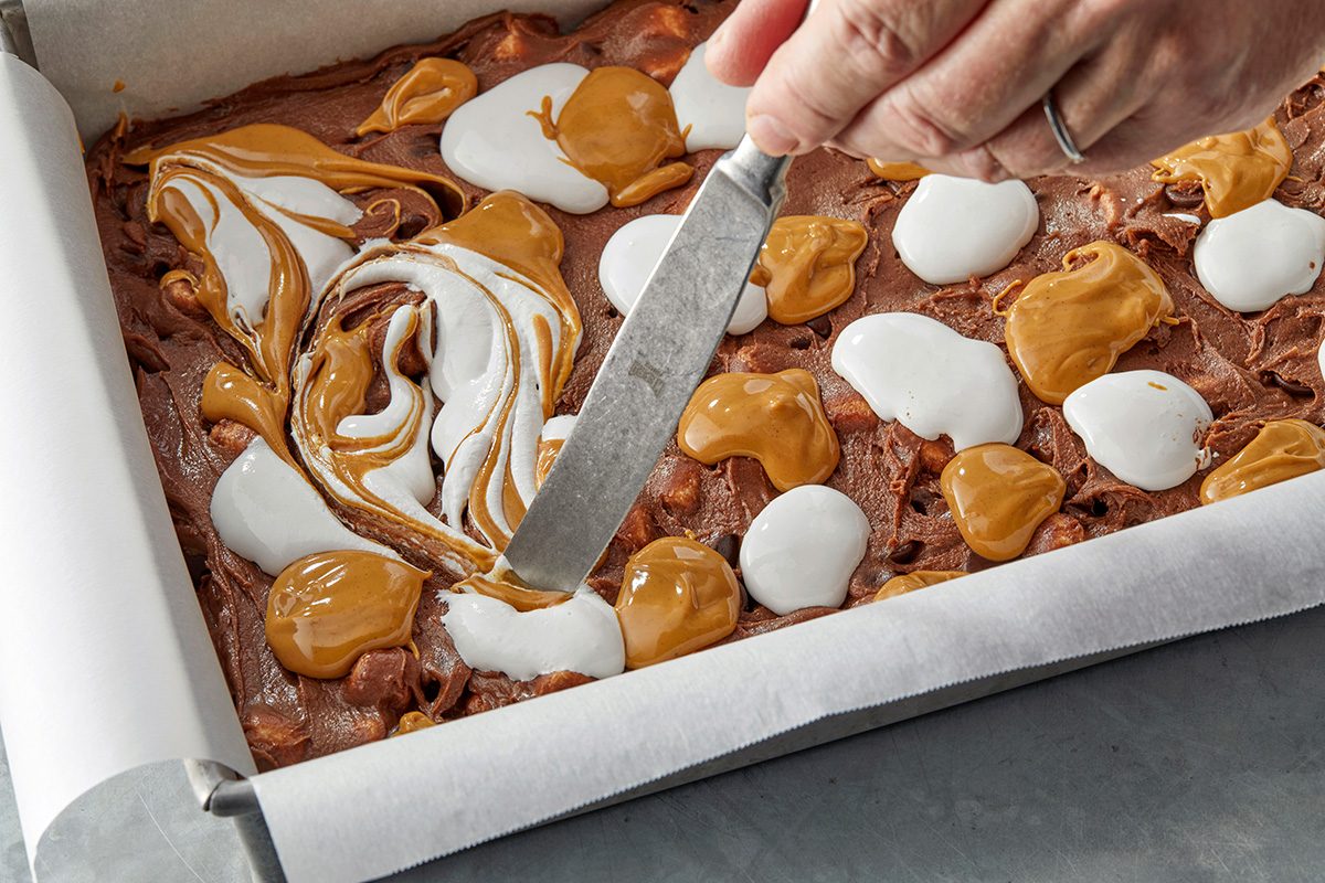 swirl together caramel and marshmallow cream toppings on a pan of brownies using knife