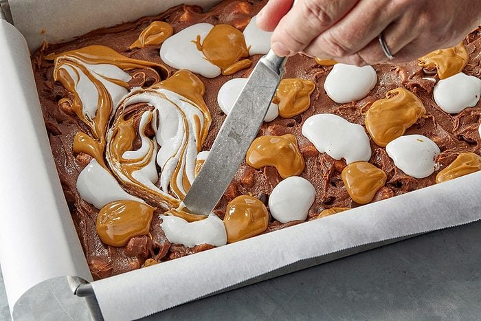 swirl together caramel and marshmallow cream toppings on a pan of brownies using knife