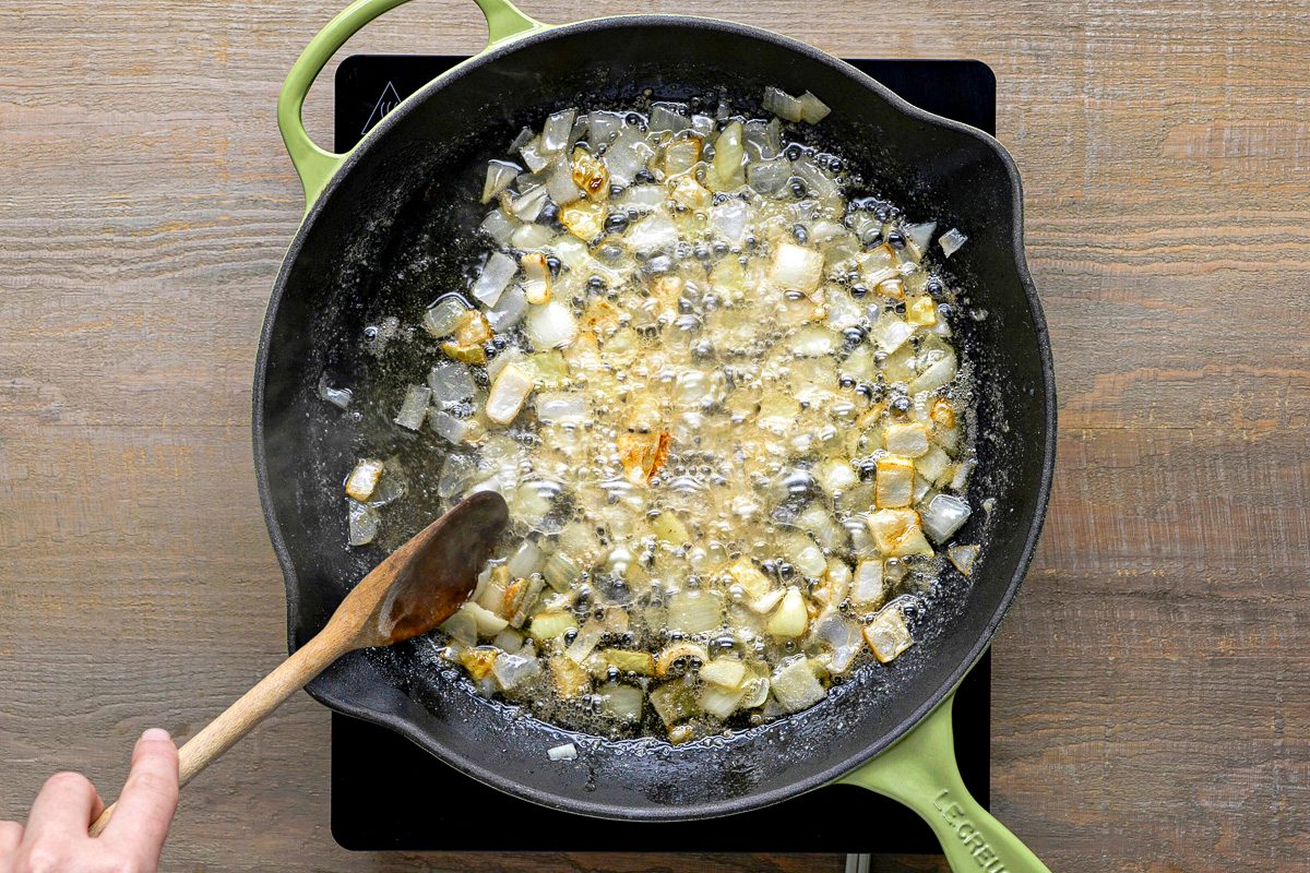 onions being cooked in a large skillet with butter and bacon fat