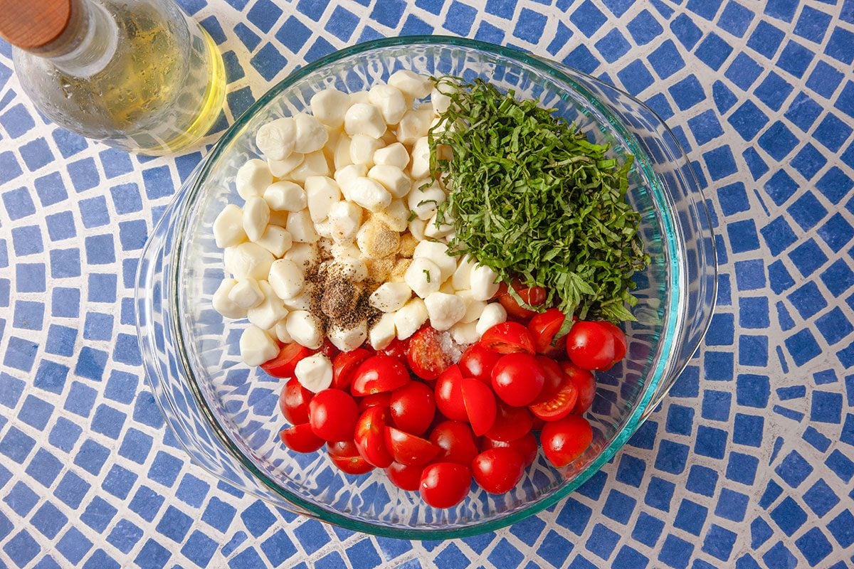Cherry tomatoes, fresh mozzarella, basil, and seasonings are combined in a bowl to prepare a gnocchi Caprese salad.