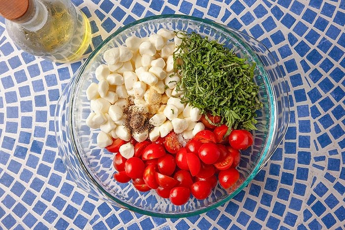 Cherry tomatoes, fresh mozzarella, basil, and seasonings are combined in a bowl to prepare a gnocchi Caprese salad.