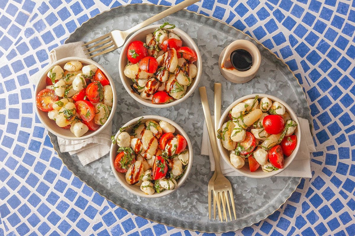 Multiple bowls of gnocchi Caprese salad are arranged on a platter for serving.