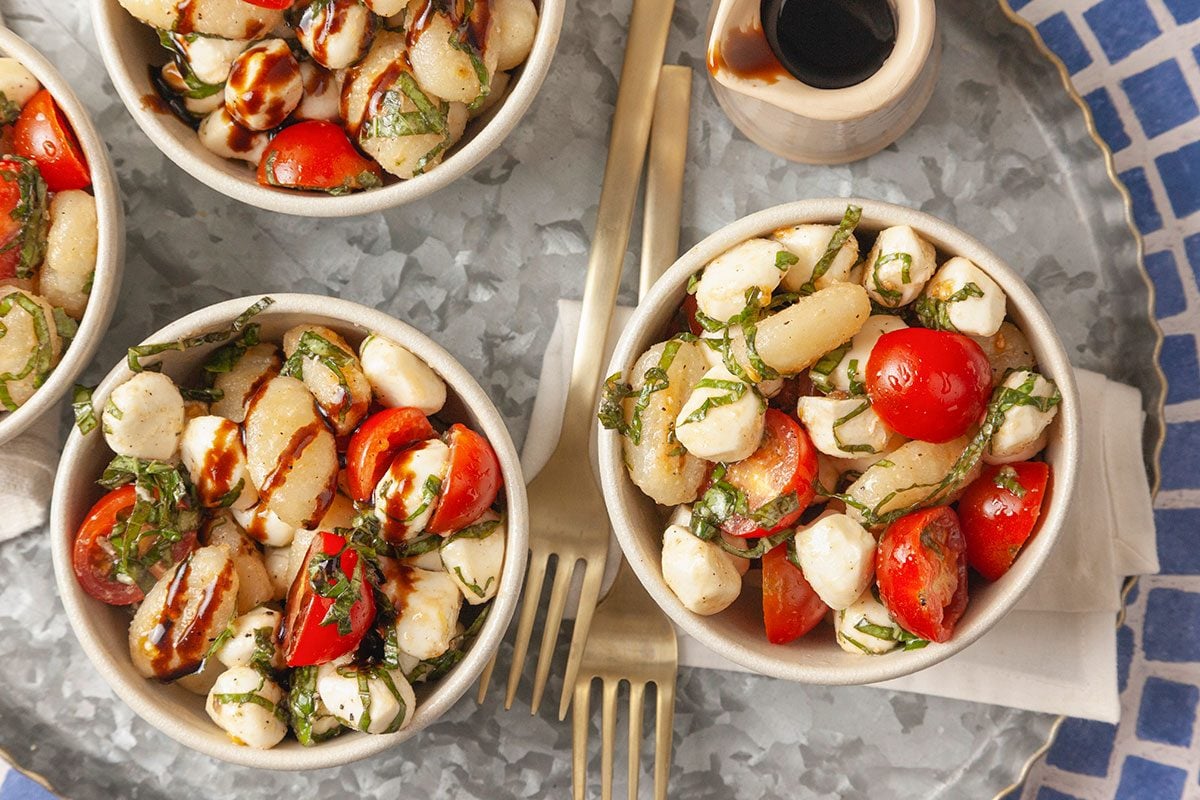 A close-up of gnocchi Caprese salad drizzled with balsamic glaze highlights the fresh ingredients and texture.