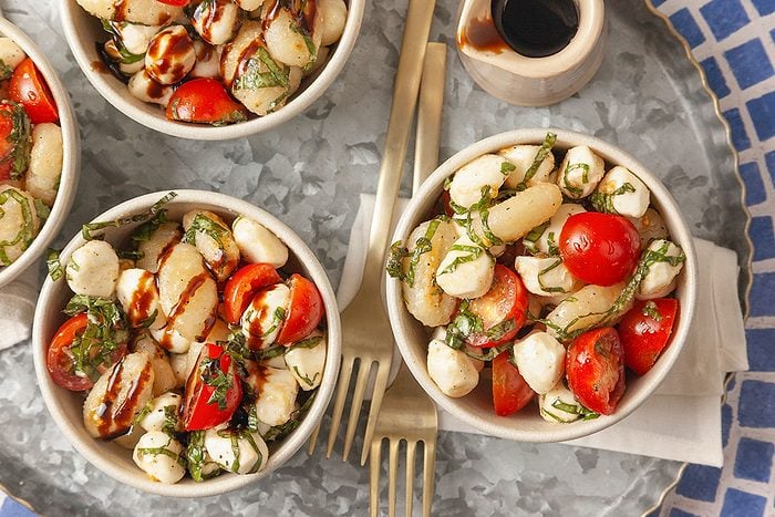 A close-up of gnocchi Caprese salad drizzled with balsamic glaze highlights the fresh ingredients and texture.