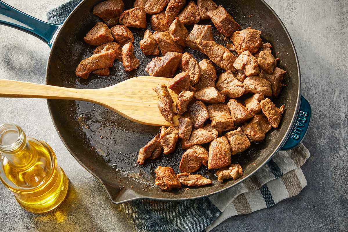 Overhead horizontal image of cubed lamb stew meat browning in a skillet with olive oil.