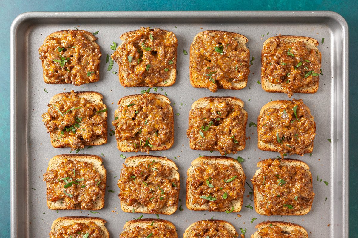 Overhead horizontal image of baked rye melts topped with chopped parsley on a sheet pan.