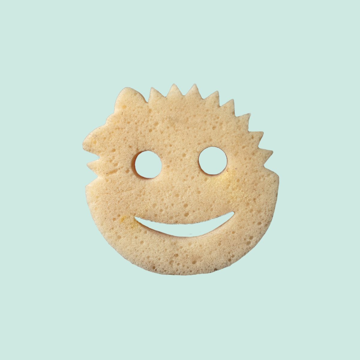 A round, beige potato snack shaped like a smiling face with spiky hair on one side, set against a light blue background. The face has two circular eye holes and a wide, curved mouth hole.