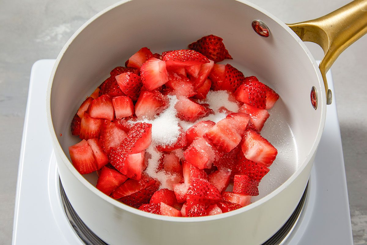 Cooking chopped fresh strawberries with sugar, salt, and water in a saucepan to create a sweet fruit base.