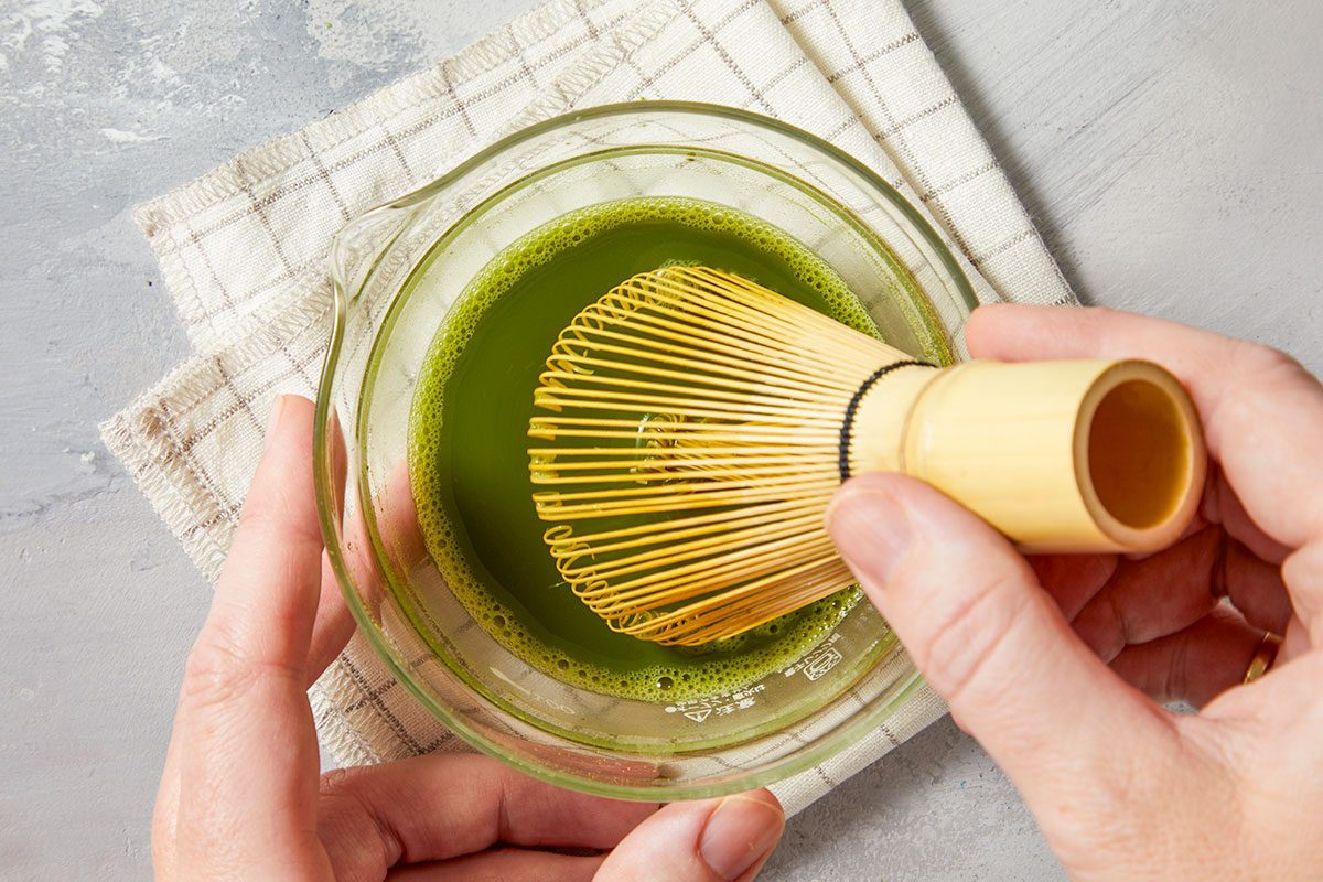 Whisking matcha powder with water in a small bowl using a bamboo whisk to create a smooth green tea mixture.