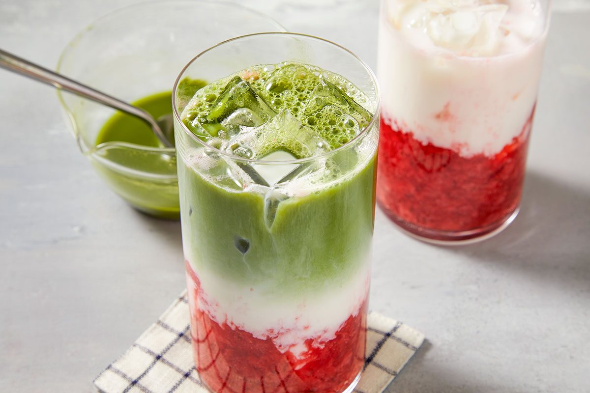 Pouring prepared matcha over ice and milk to begin layering the strawberry matcha iced latte.