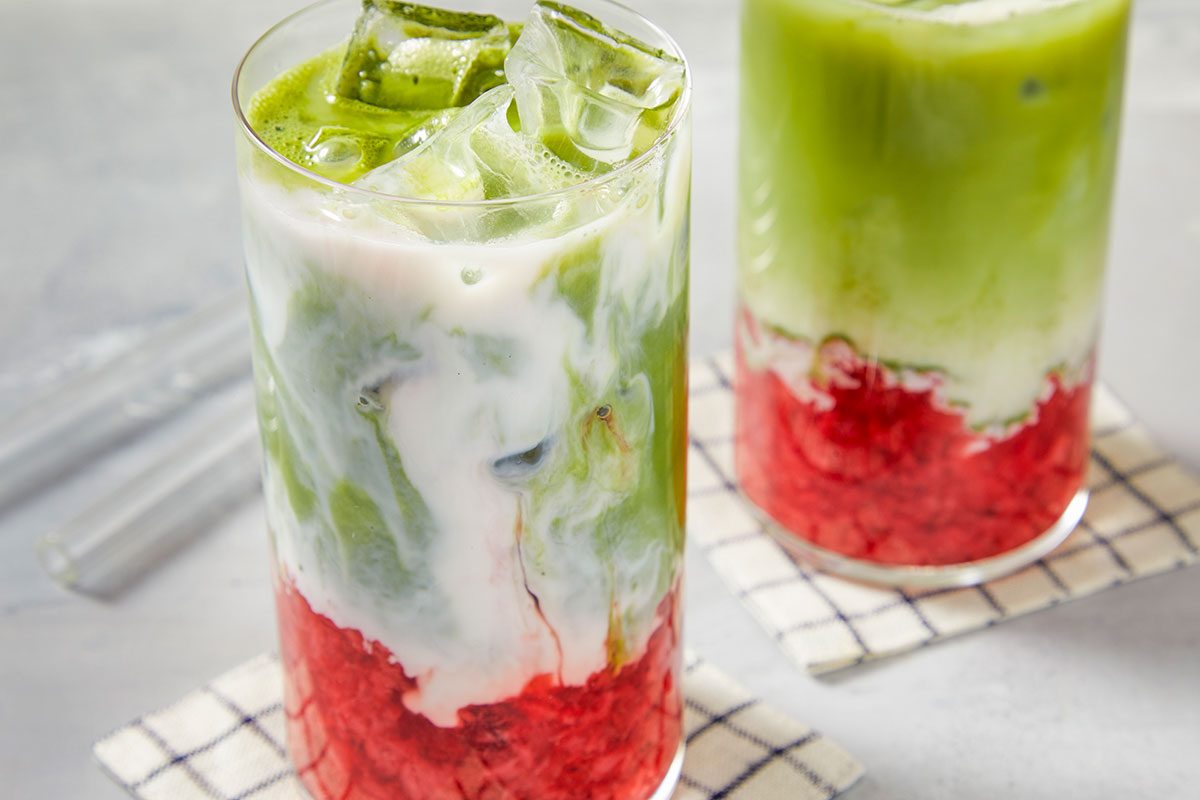 Close-up of a strawberry matcha iced latte as milk swirls into the matcha layer, creating a marbled effect.