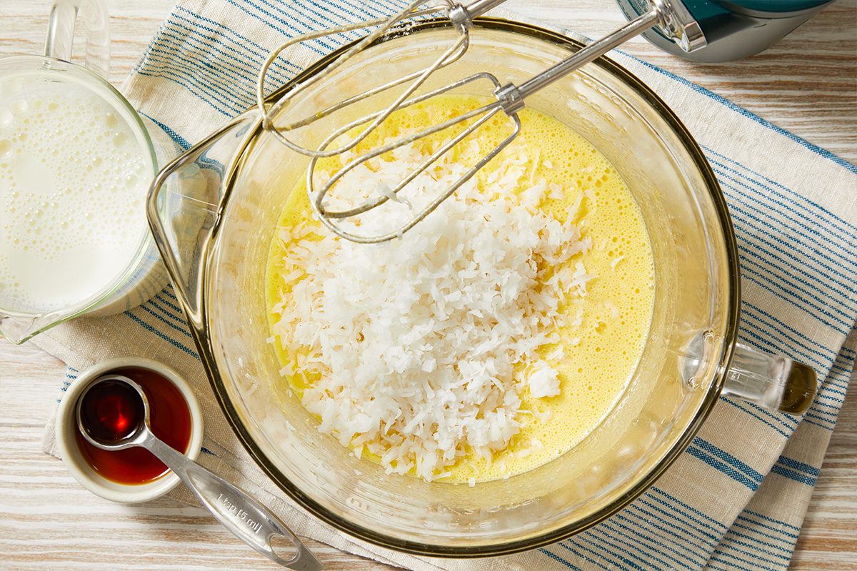 Overhead horizontal image of pie batter being mixed with coconut and wet ingredients in a glass bowl.