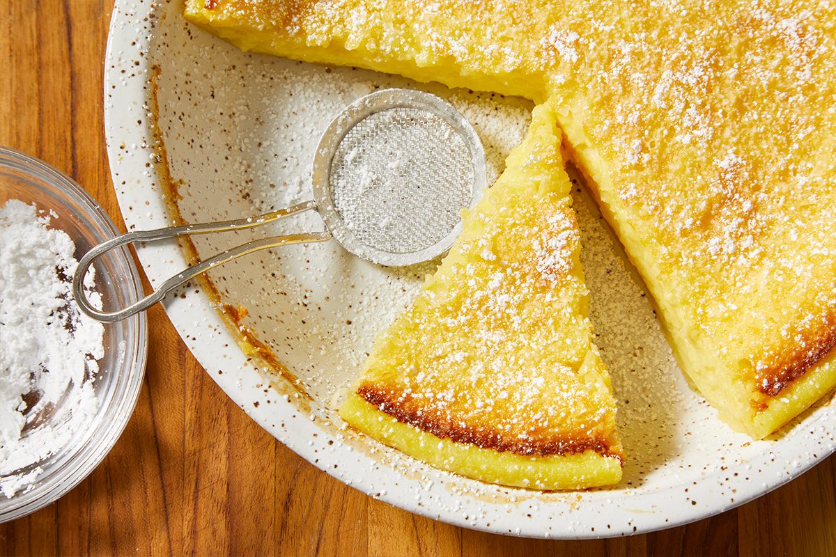 Overhead horizontal image of Impossible Pie with multiple slices cut and powdered sugar being dusted on top.