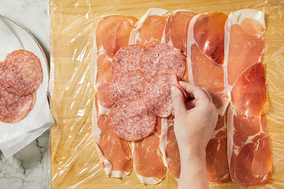 Thinly sliced prosciutto is layered on plastic wrap and topped with overlapping rounds of salami to create the base for the roll.