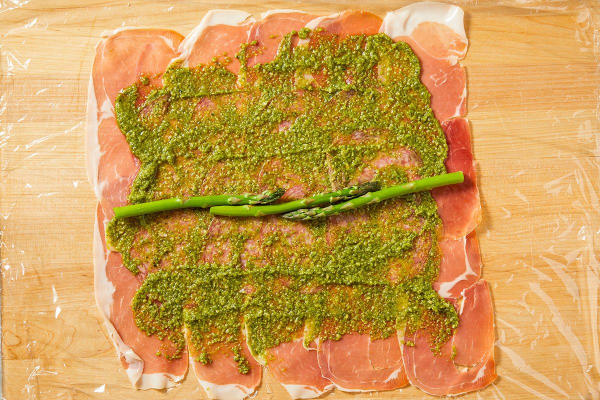 Pesto is spread evenly over the meat layer and asparagus spears are placed across the center.