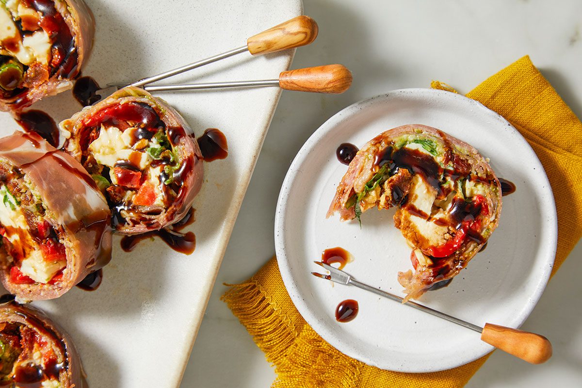 Finished Italian sushi rolls are arranged on a plate, showcasing colorful layers and garnished with balsamic glaze.