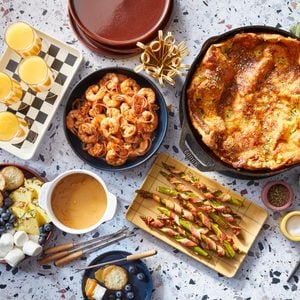 overhead image shows multiple brunch dishes including shrimp, Dutch baby, asparagus, mimosas, and dulce de leche arranged together.