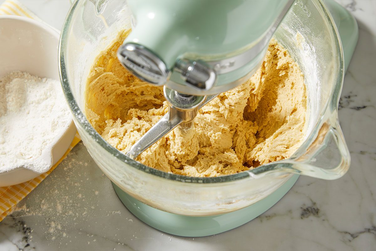 A horizontal overhead image shows thick cookie dough forming in a stand mixer with flour and dry ingredients being incorporated.