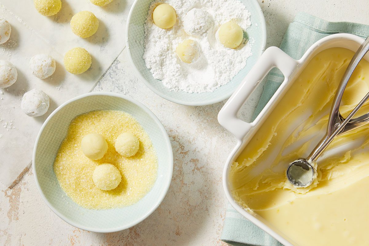 Overhead horizontal image of scooped truffle balls being rolled in sugar coatings.