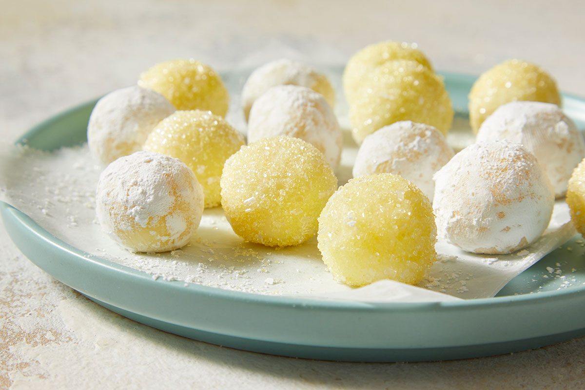 Eye-level horizontal image of lemon truffles served on a plate with powdered sugar and coarse sugar coating.
