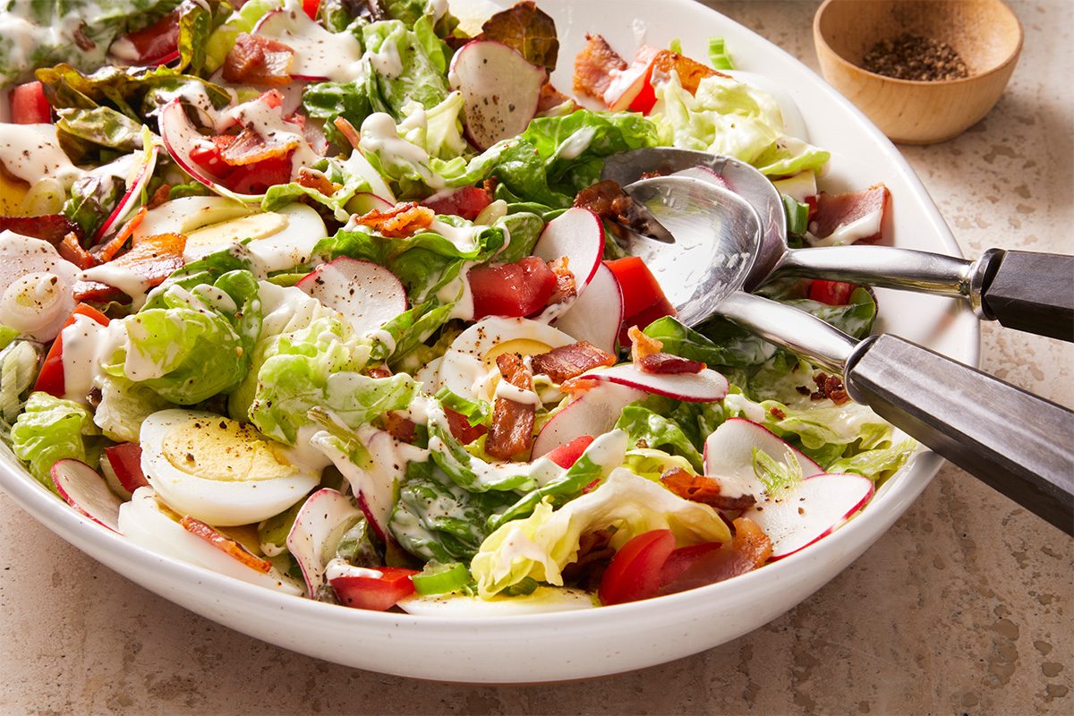 3/4 shot of the Garden Lettuce Salad in a wide white serving bowl with silver spoon.