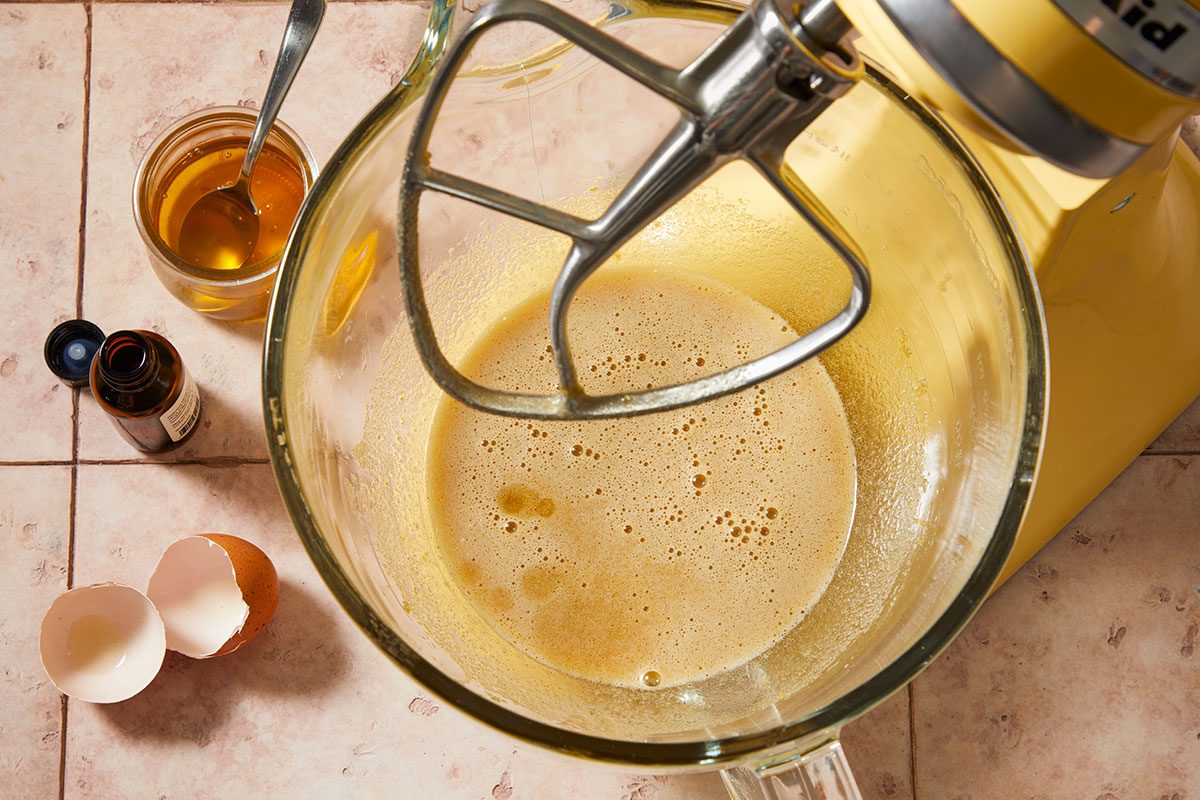 Overhead horizontal step-by-step image of wet ingredients including egg, oil, honey, and lemon extract being mixed in a stand mixer bowl.