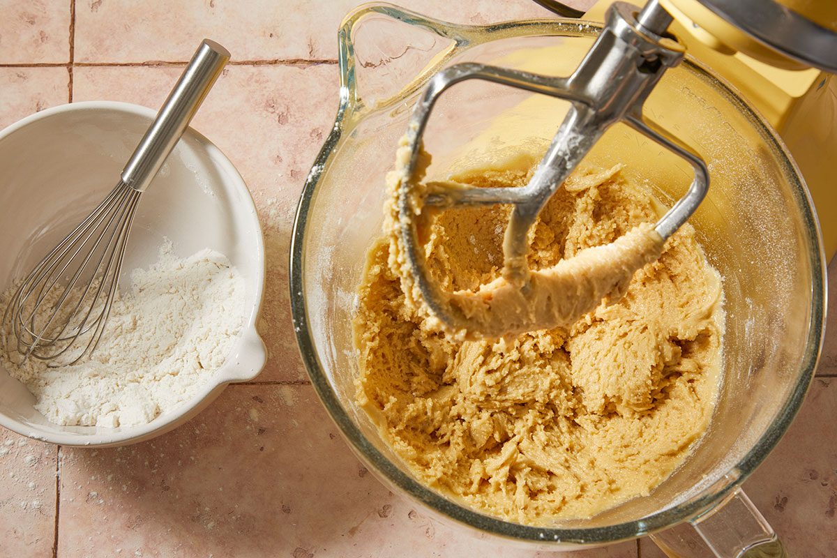 Overhead horizontal step-by-step image of dry ingredients being incorporated into cookie dough in stand mixer.