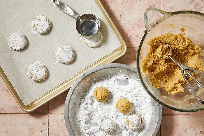 Overhead horizontal step-by-step image of portioned cookie dough balls rolled in confectioners' sugar on baking sheet.