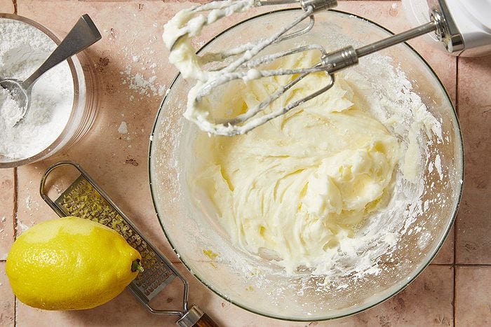 Overhead horizontal step-by-step image of lemon buttercream filling being mixed with lemon zest in a bowl.