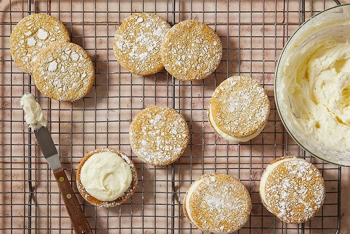 Overhead horizontal push and pulls image of baked crinkle cookies being filled with lemon buttercream on cooling rack.