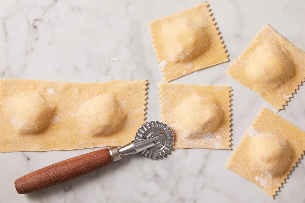 Cut lobster ravioli pieces arranged on a marble countertop after being sealed and trimmed with a fluted pasta cutter wheel. The square ravioli show the lobster filling beneath the thin pasta dough.