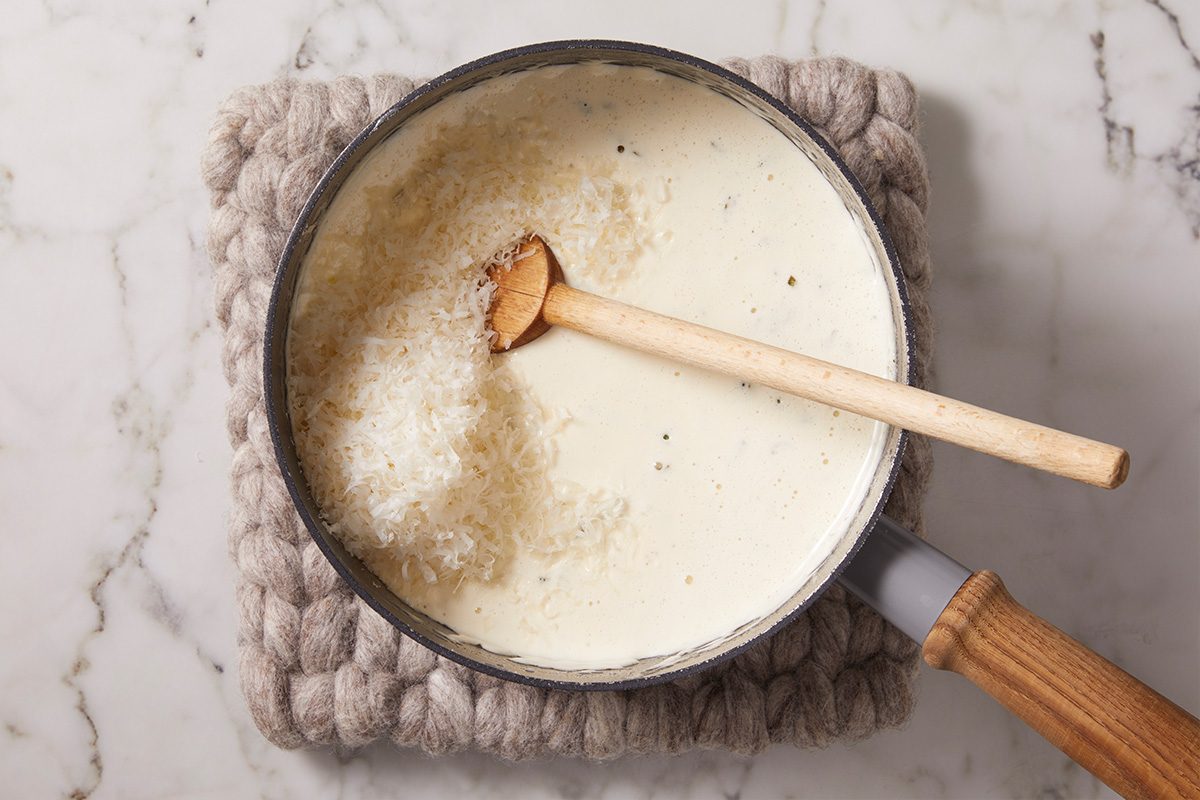 Cream sauce being prepared in a saucepan with butter, garlic, white wine and heavy cream simmering together to create a rich sauce for lobster ravioli.