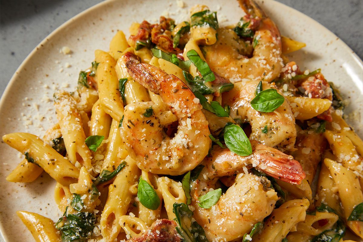 Eye Level horizontal image of Shrimp Pasta on a plate. The shrimp and pasta are tossed together with herbs, tomatoes, and grated cheese.