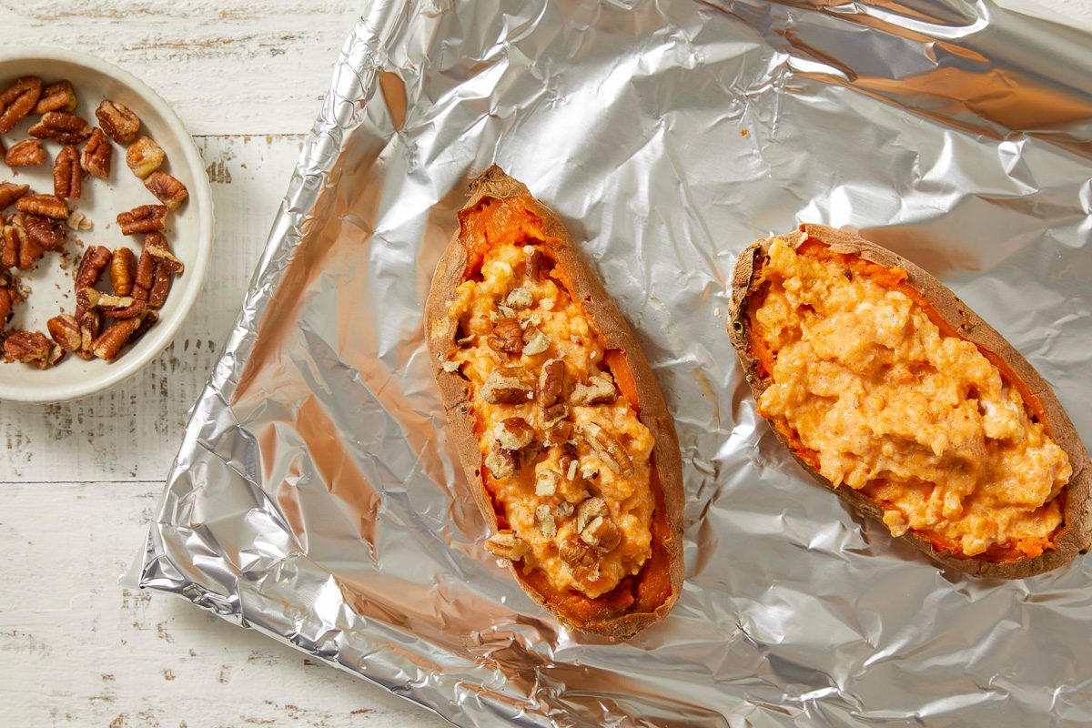 potato shells with filling and top with chopped pecans on a tray covered in aluminum foil