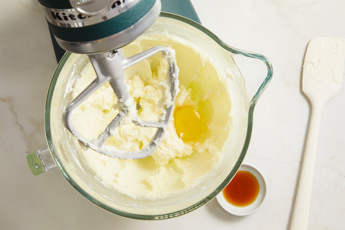 Overhead horizontal image of butter, cream cheese, sugar, and egg being mixed in a stand mixer.