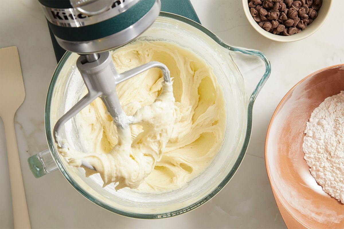Overhead horizontal image of smooth cookie dough being mixed with chocolate chips in a stand mixer.