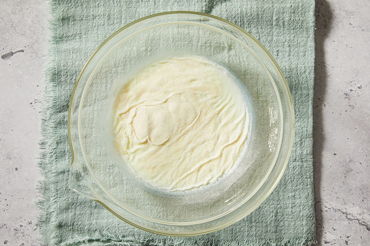 Overhead horizontal image of gelatin blooming in milk in a glass bowl on a textured surface.