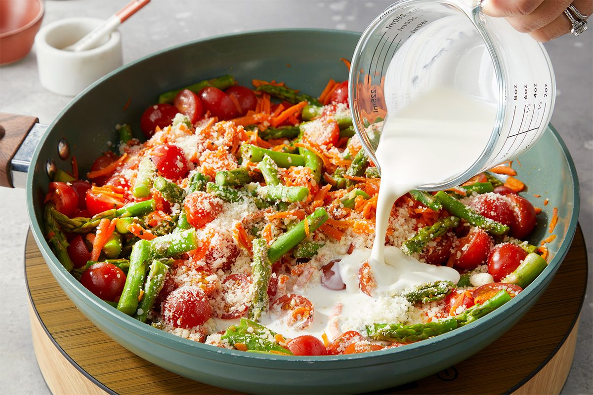 Heavy cream is poured into the skillet with vegetables, tomatoes, and Parmesan to create a creamy sauce.