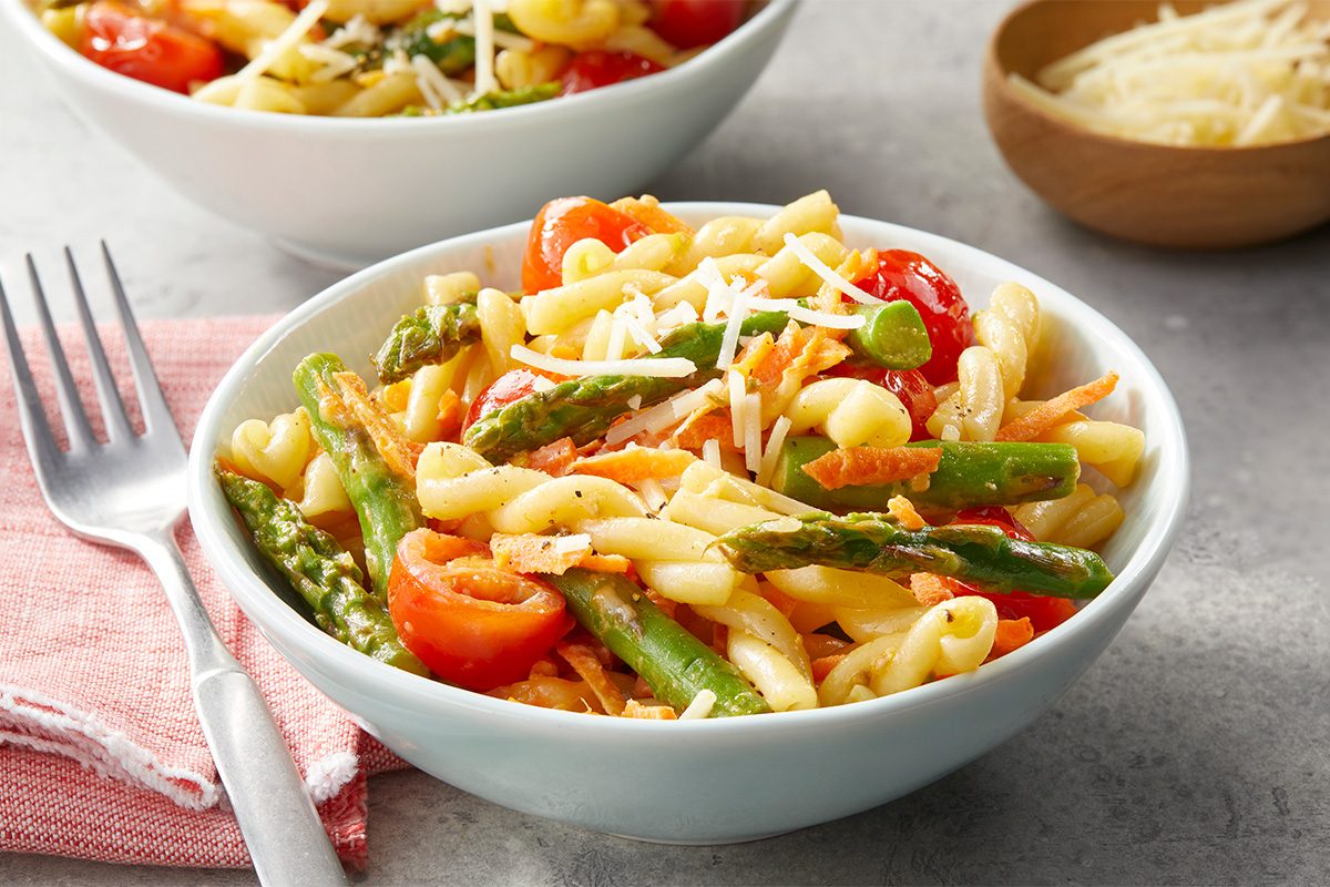 A bowl of creamy pasta primavera is presented with visible vegetables and grated Parmesan in a simple setting.