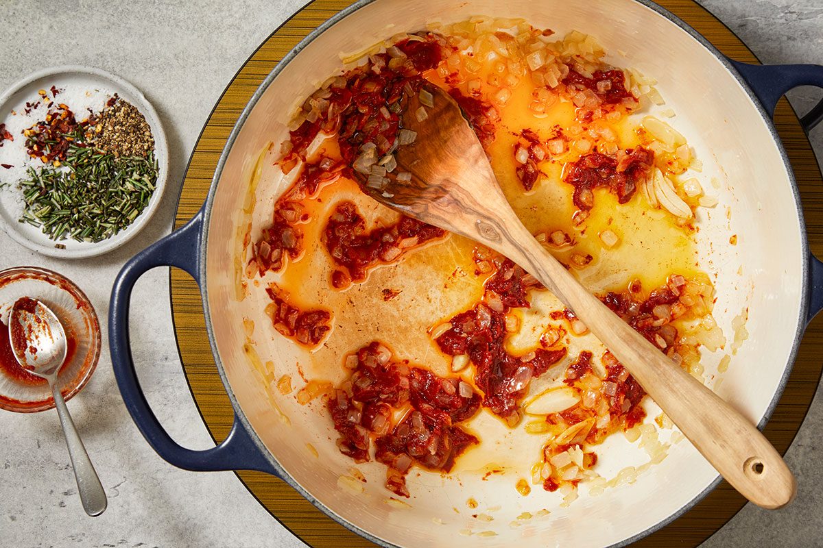 Overhead horizontal image of aromatics and tomato paste sautéing in olive oil in a Dutch oven to begin pasta e ceci.