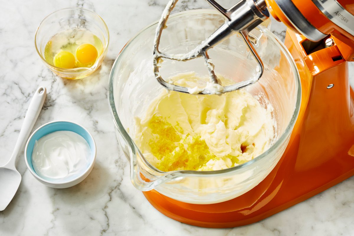 Overhead view of softened butter and sugar being mixed in a glass bowl with a stand mixer, beginning preparation of peach cookie dough on a marble surface.