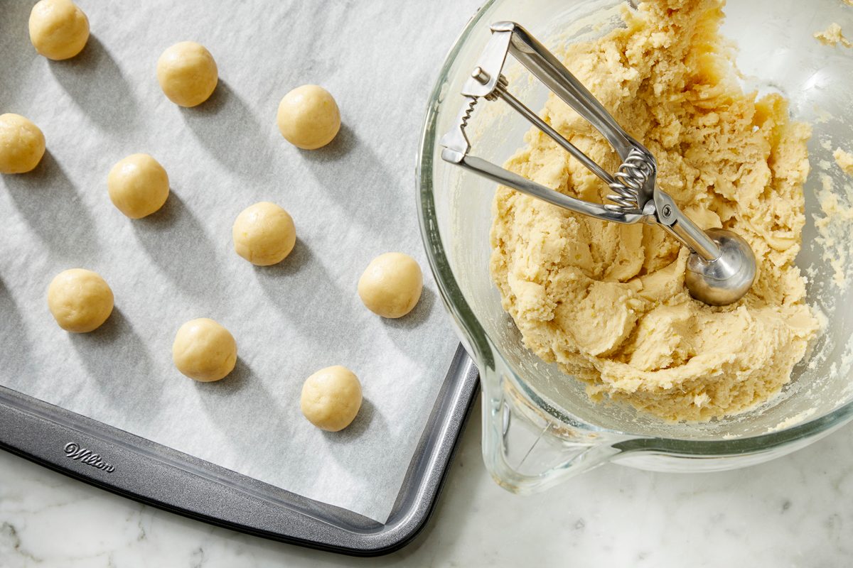 Overhead view of peach cookie dough portioned into small balls and arranged on a parchment-lined baking sheet.