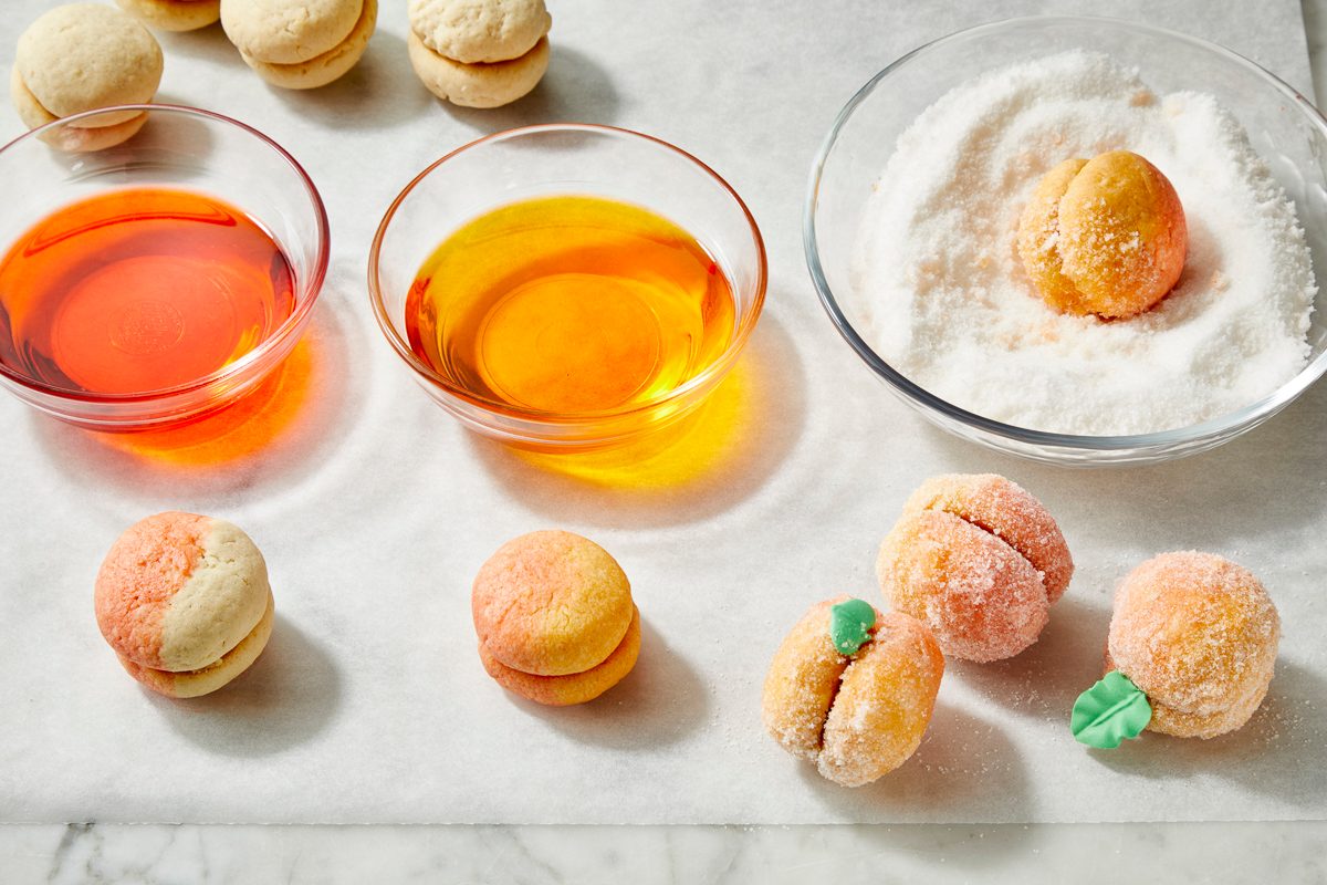 Overhead view of peach-shaped cookies dipped in colored peach schnapps and coated in sugar for decoration.
