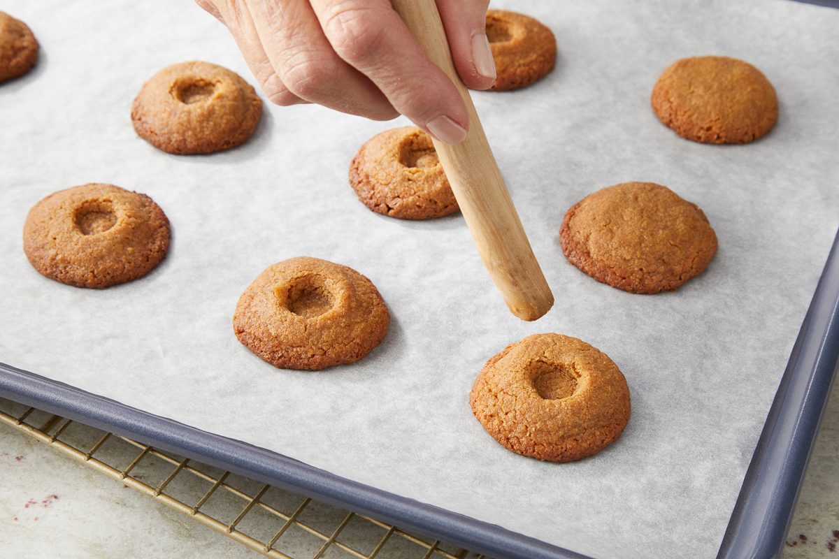 Pressing indentations in the center of each cookie with the end of a wooden spoon handle