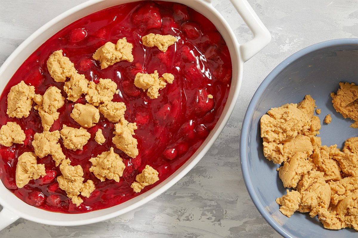 Overhead horizontal step-by-step image of peanut butter cookie dough crumbled over strawberry filling in baking dish.